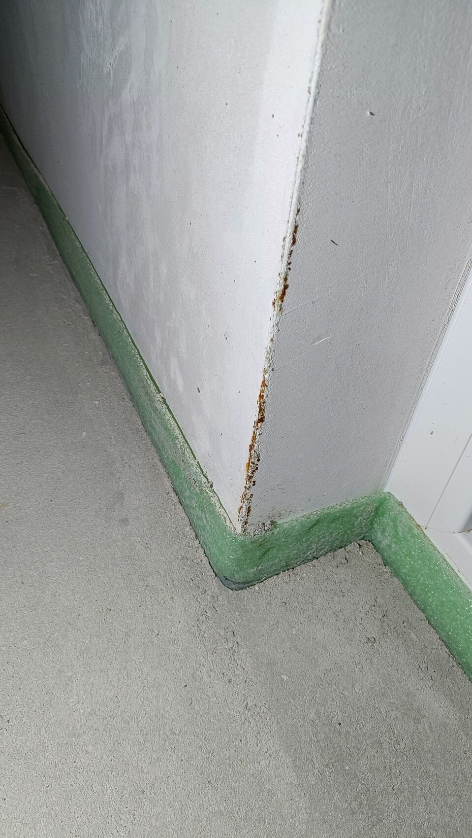 Eckbereich: grauer Boden, weiße Wand, grüne Sockelleiste, rostige Spalte an der Wandkante