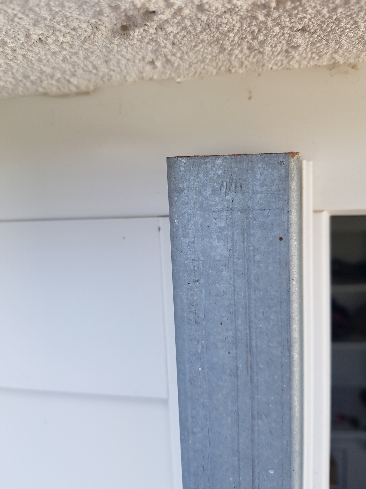 Vertikaler, grauer galvanisierter Metallpfosten neben der Türöffnung; rostige Oberkante sichtbar.
