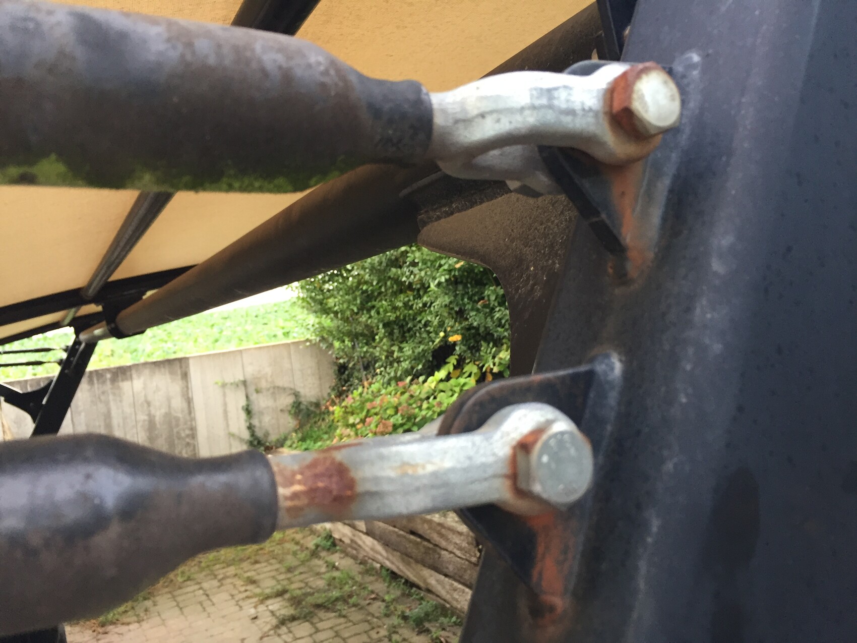 Nahaufnahme eines rostigen Bolzens an einem Metallarm am Rahmen; Garten im Hintergrund.