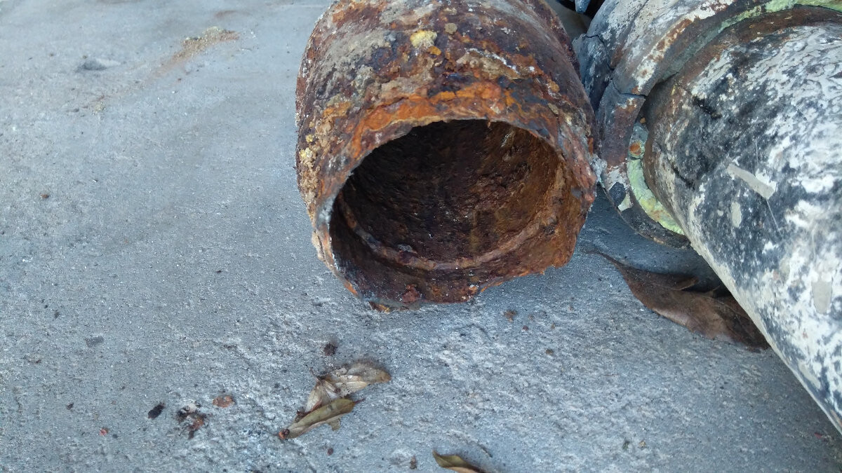Rostiges, offenes Metallrohr auf Betonboden; stark verrostet und innen hohl.