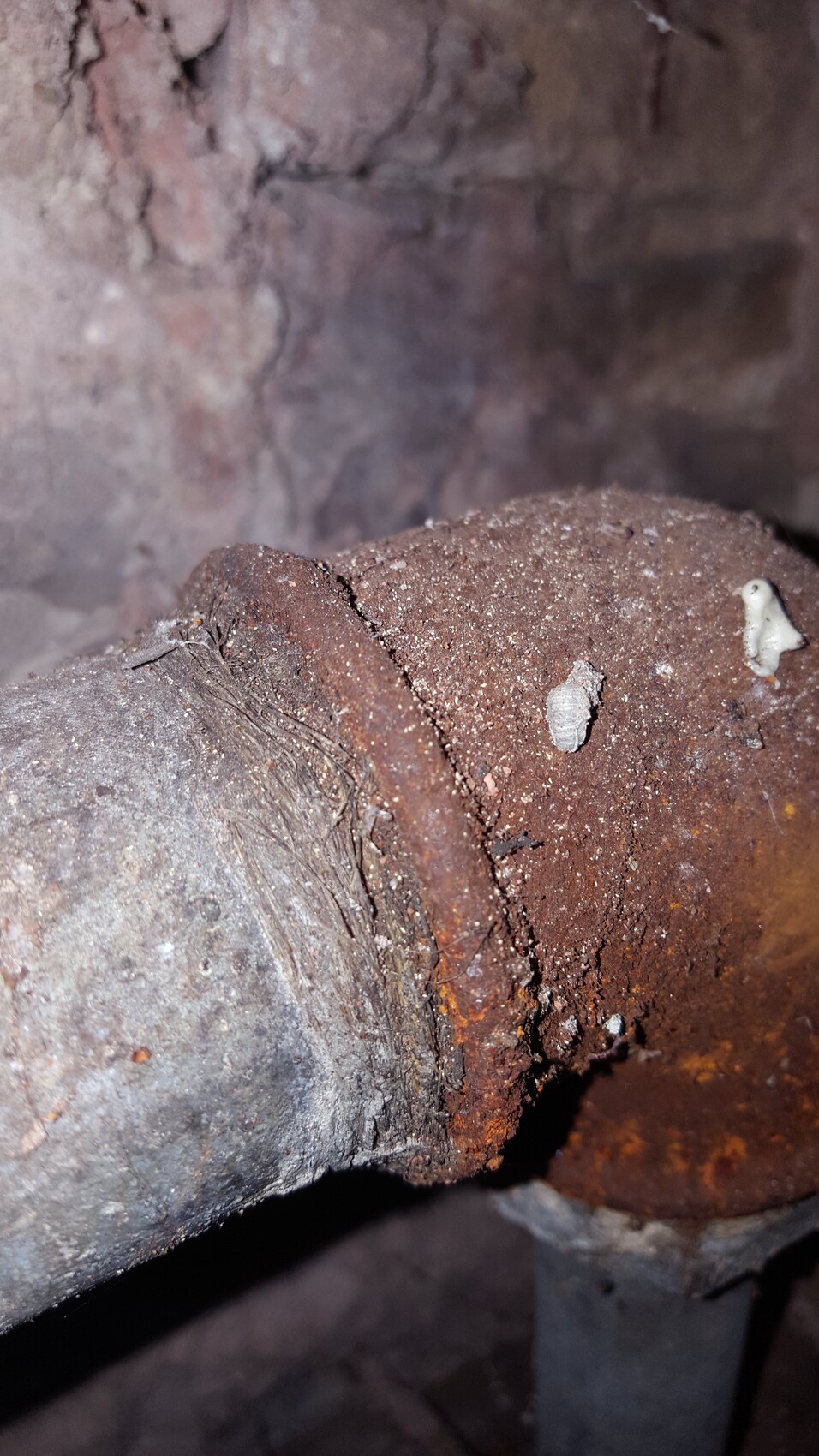 Rostige Metallleitung mit Riss, Staub und rauer Steinwand im Hintergrund.