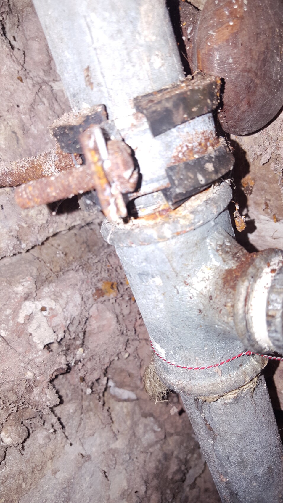Verrostete Rohrschelle an einem Metallrohr im staubigen Erdreich.