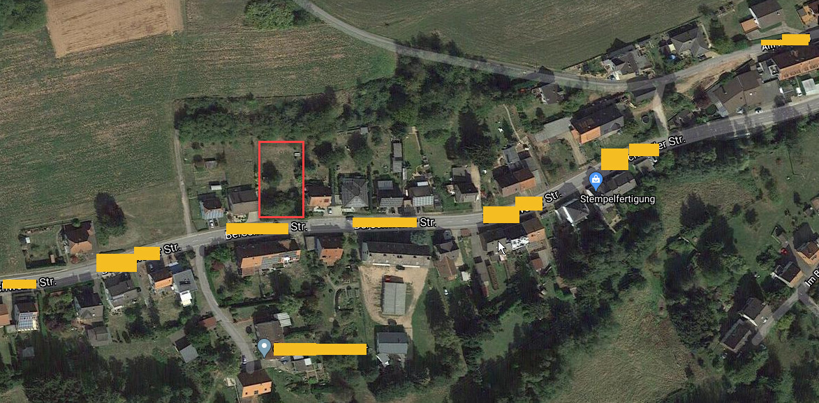 Luftbild eines Dorfes: rotes Rechteck markiert unbebautes Grundstück, gelbe Markierungen der Straße.