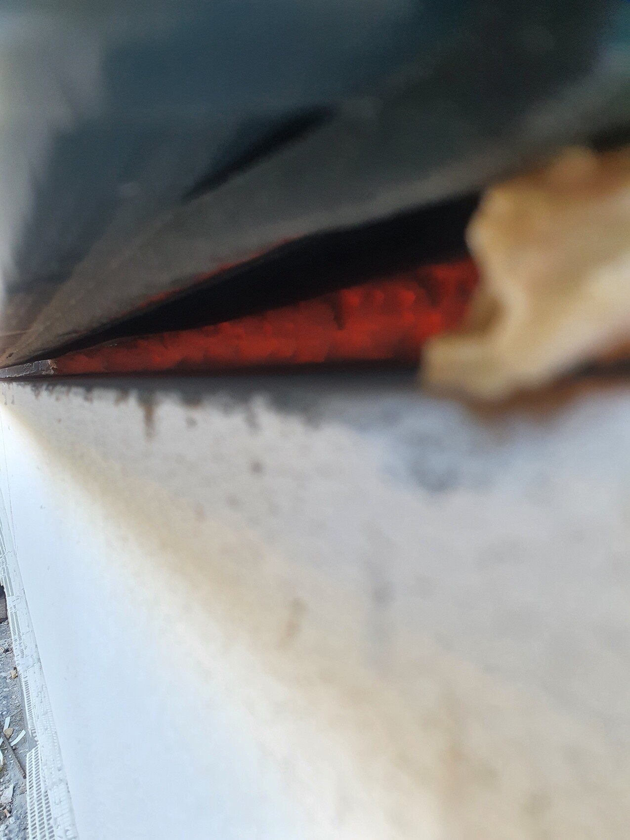 Nahaufnahme eines Spalts zwischen dunkler Metallplatte und roter Innenfläche.