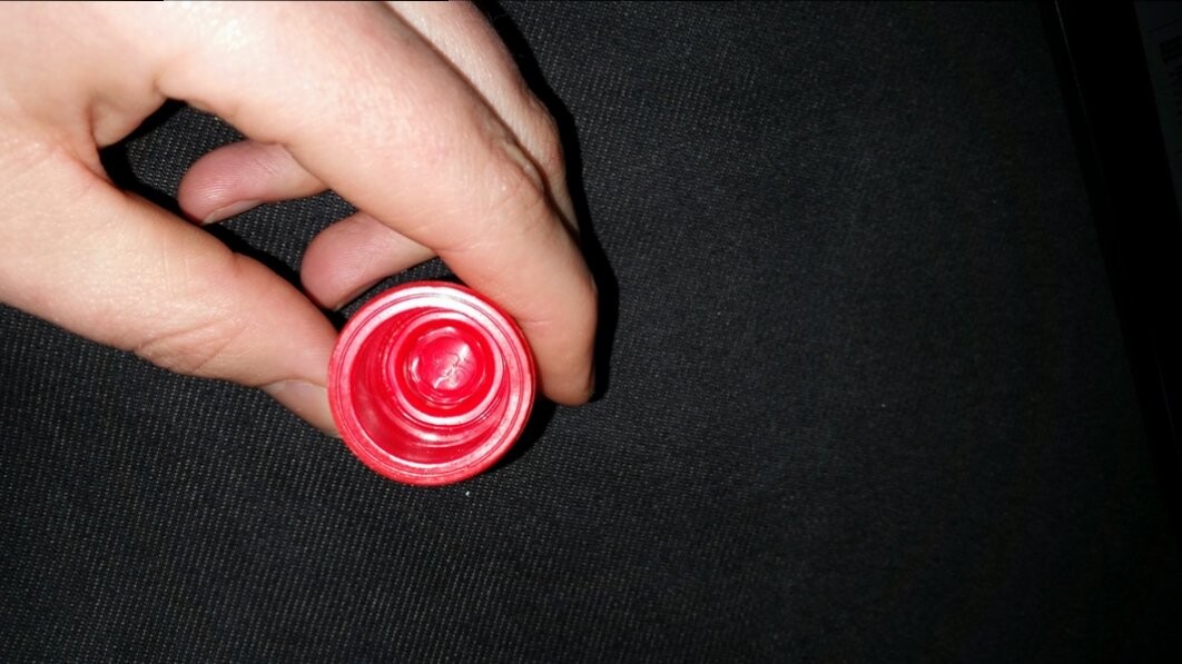 Rote Flaschenkappe wird von Hand vor dunklem Hintergrund gehalten.