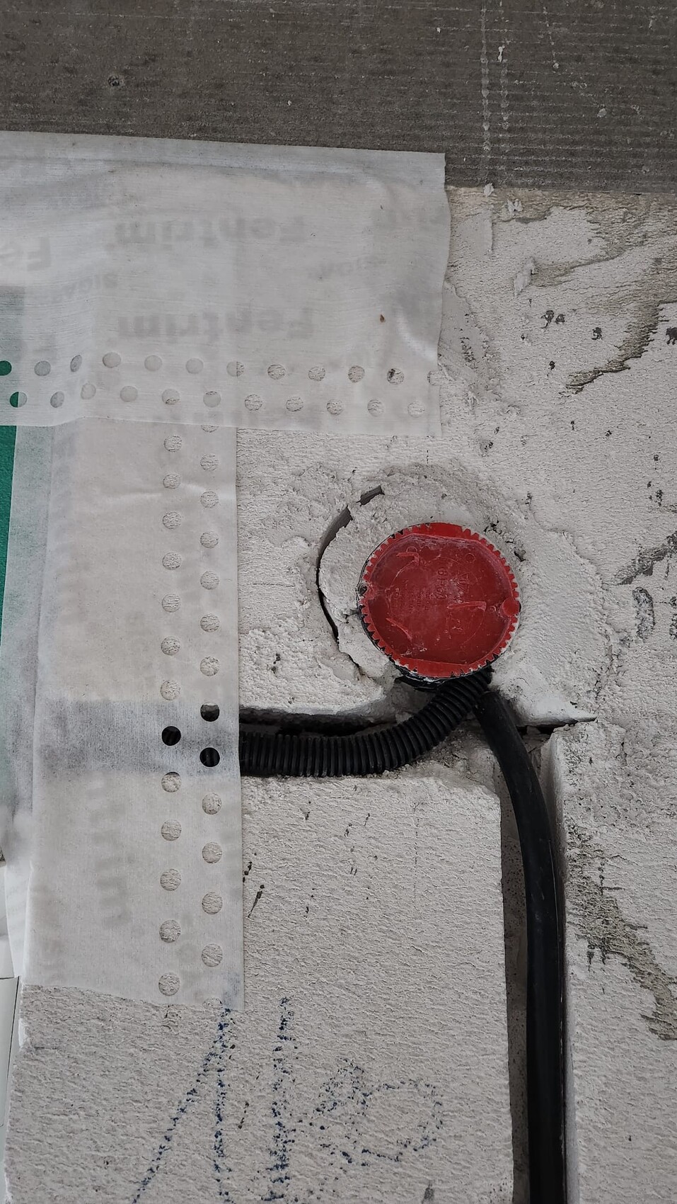Roter Deckel in Wandöffnung, daneben schwarzes Kabelrohr und Putzreste.