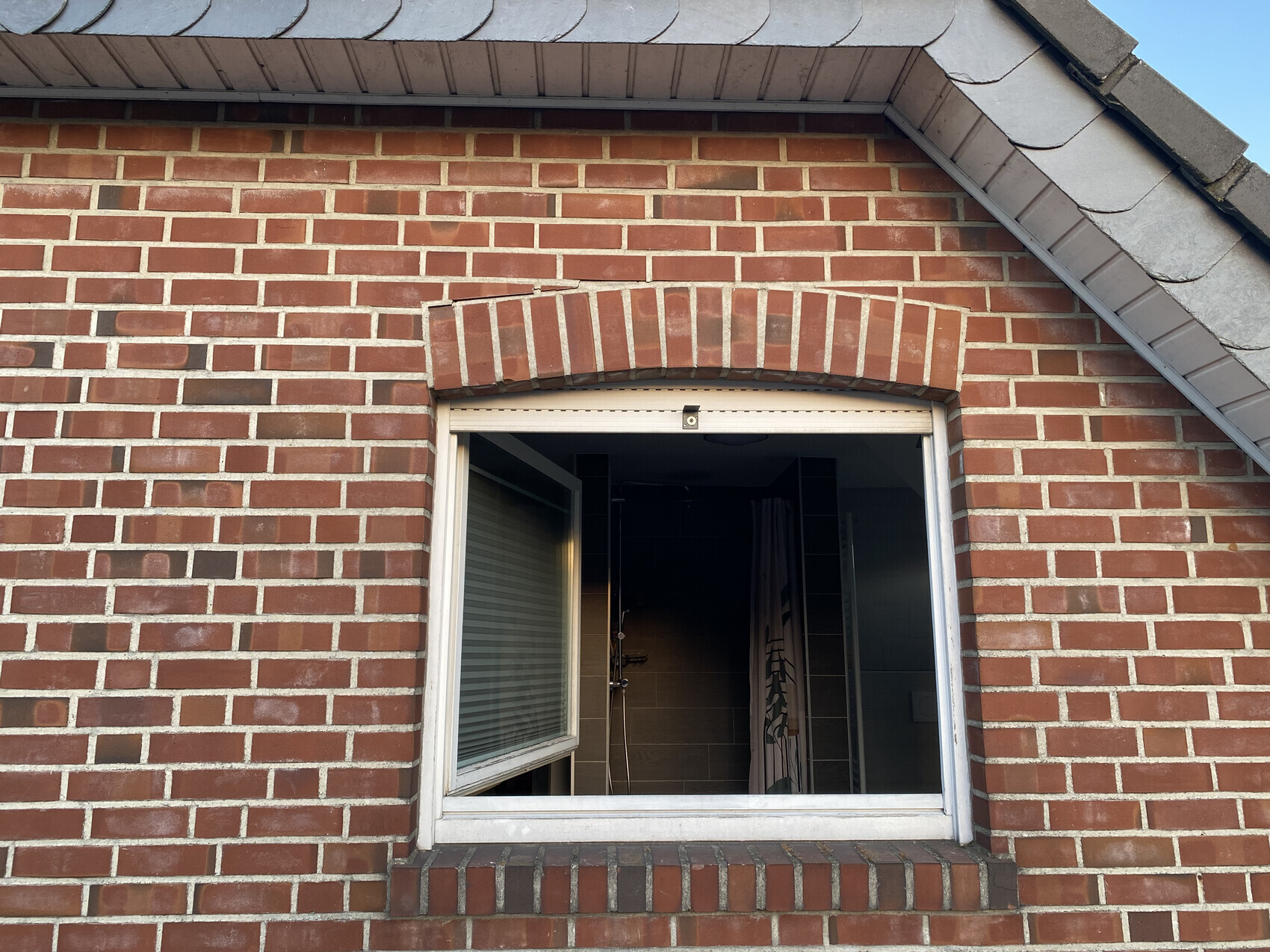 Offenes Badezimmerfenster in roter Backsteinfassade, Innenraum mit Dusche.