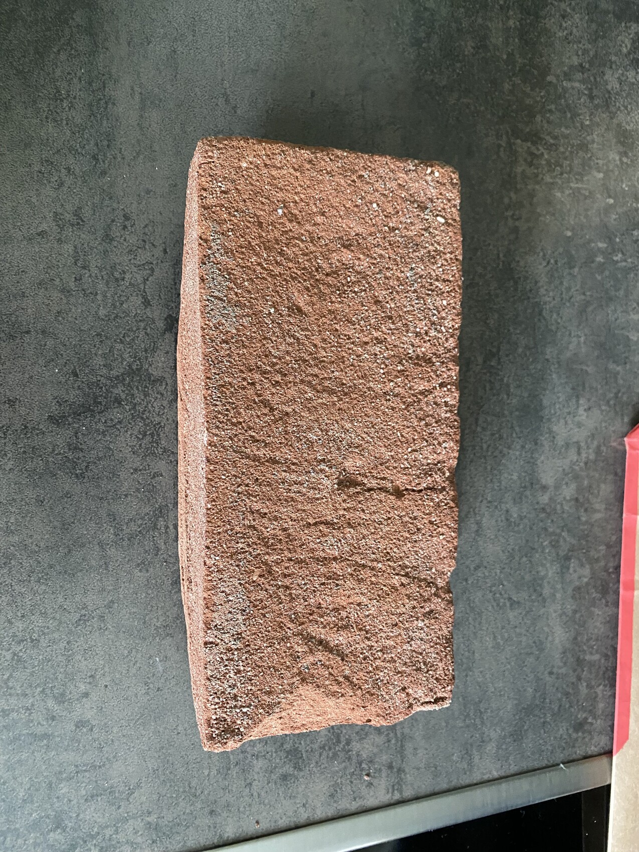 Roter Backstein mit rauer Oberfläche liegt auf dunklem Hintergrund.