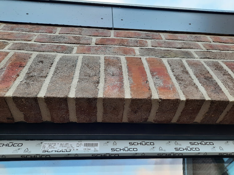 Außenansicht einer Backsteinfassade mit Fensterrahmen; Schutzband SCHÜCO am Rahmen.