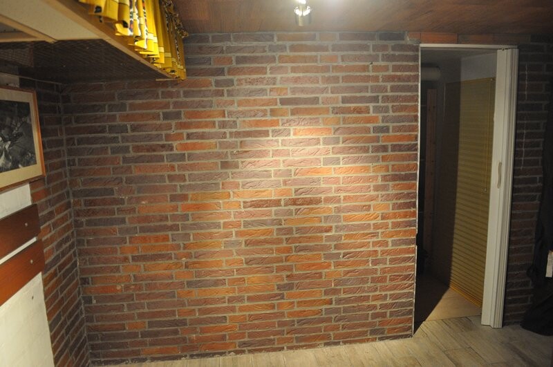 Innenraum mit Ziegelwand, Holzboden; Tür rechts ins Nebenzimmer, links Gelbregal.