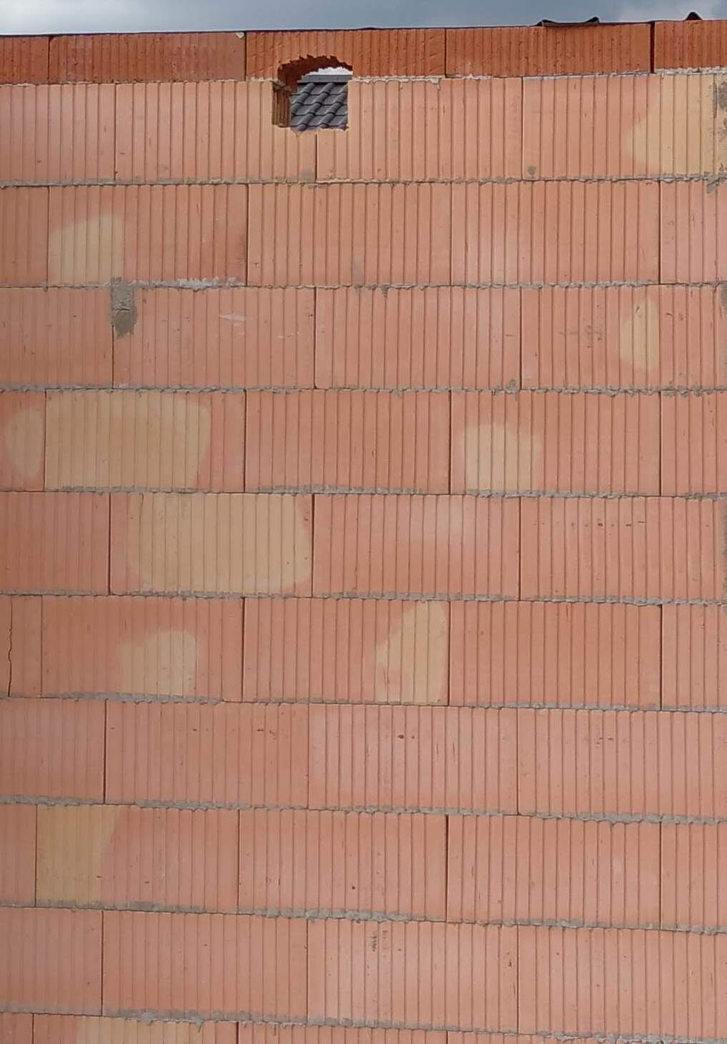 Rote Ziegelwand mit kleinem Oberloch; dahinter sind dunkle Dachziegel zu sehen.
