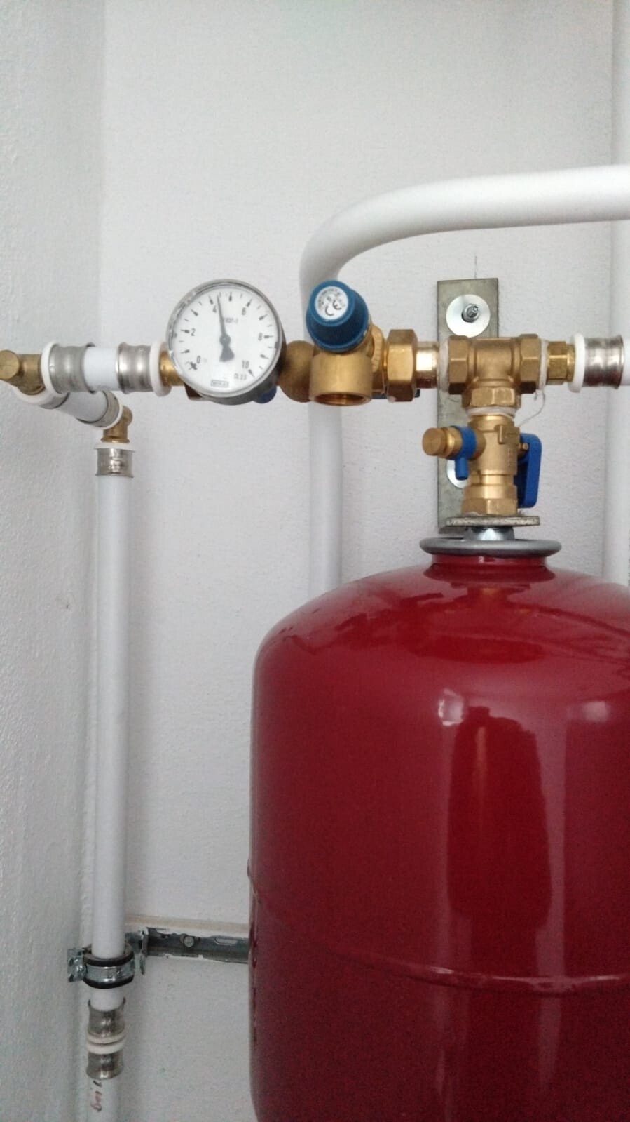 Roter Ausdehnungsbehälter in einer Heizungsanlage, verbunden mit Druckmessgerät und Kupferarmaturen.