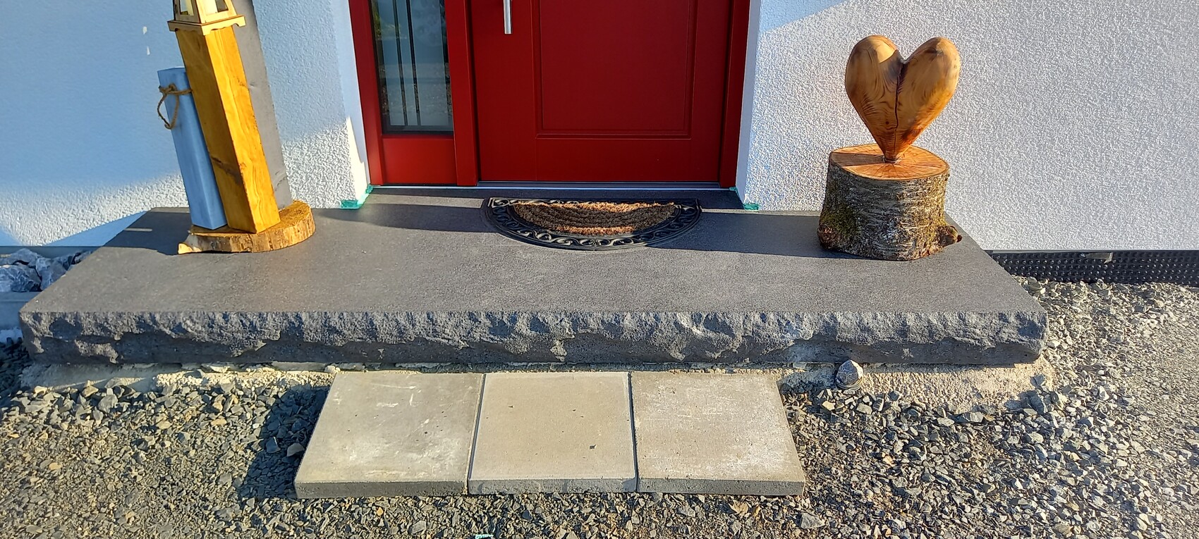 Außenaufnahme eines roten Haustür-Eingangs mit massiver Steinplatte und Holzkulptur.