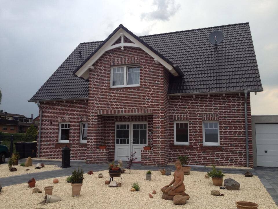 Ziegelhaus mit dunklem Satteldach, zweistöckig, Kiesgarten mit Topfpflanzen, Steinfigur und Garage.