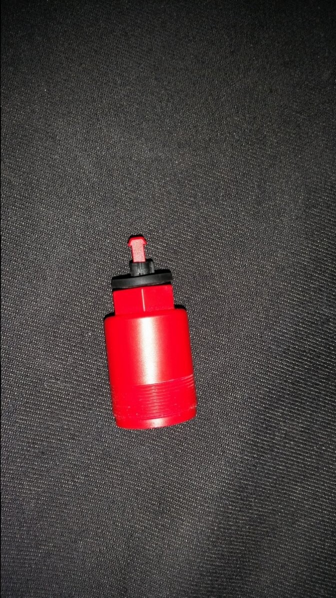 Kleines rotes Kunststoffteil mit schwarzer Kappe auf dunklem Stoffhintergrund