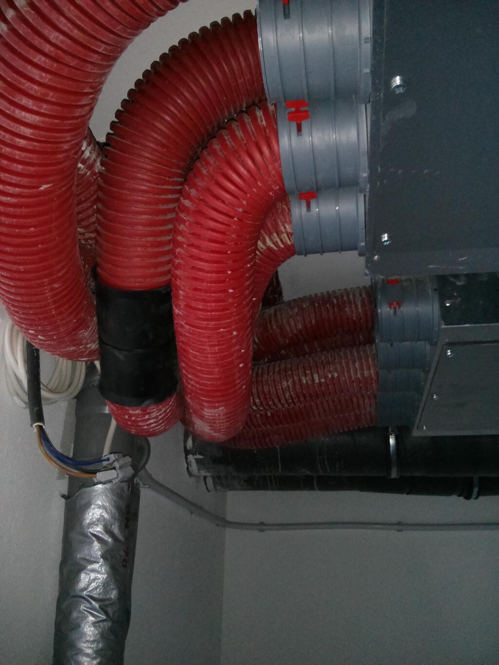 Rote flexible Lüftungsschläuche umgeben eine graue HVAC-Einheit in einem Technikraum.