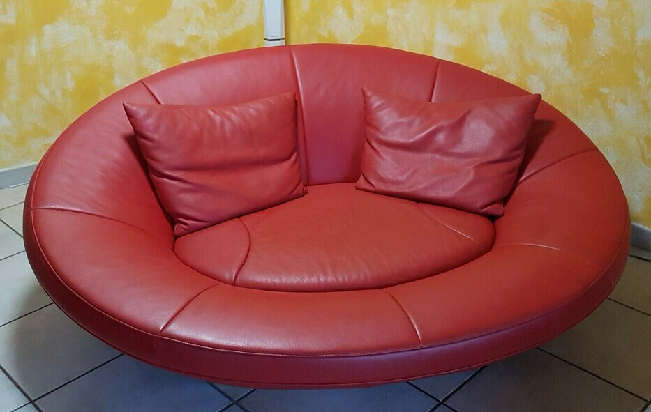 Rundes rotes Ledersofa mit zwei Kissen vor gelber Wand