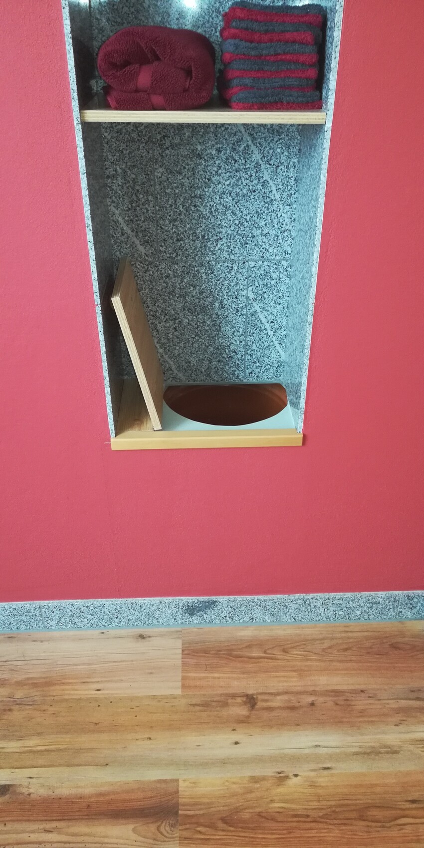 Rote Badezimmerwand mit offener Nische aus Granit, gestapelte Handtücher im Regal