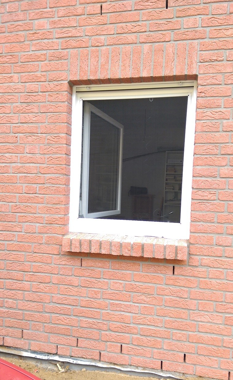 Offenes Fenster in roter Ziegelwand, Blick ins Innenraum mit Schränken und Regal.