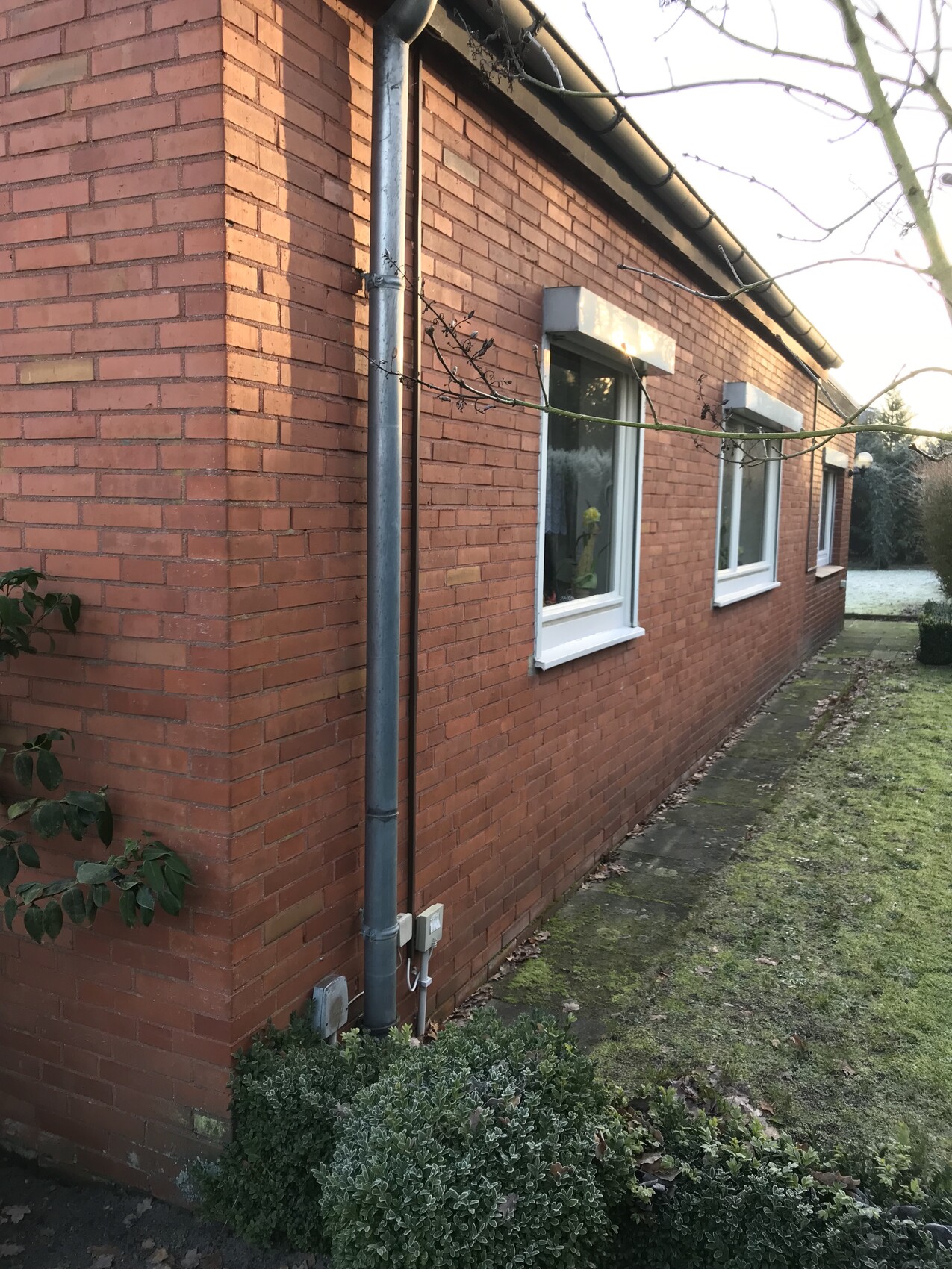 Außenansicht eines roten Ziegelhauses mit weißen Fensterrahmen und Dachrinne