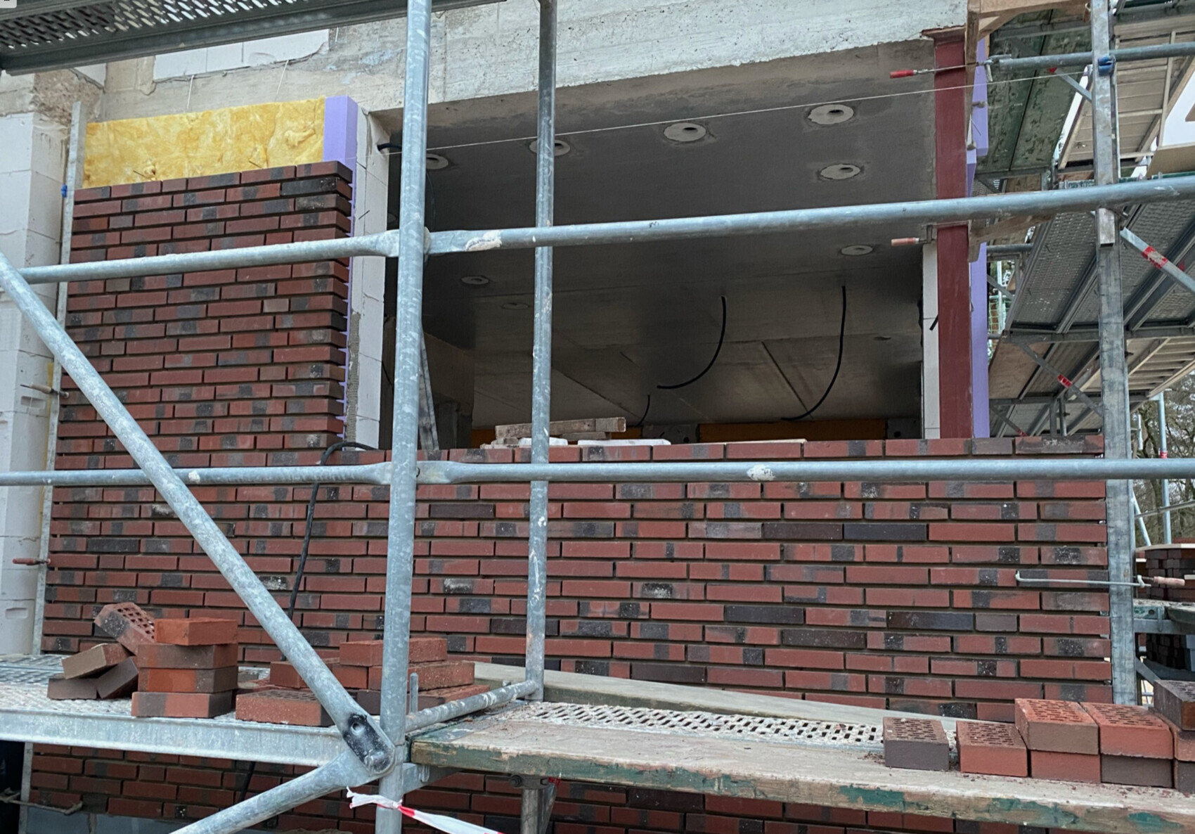 Gerüst vor roter Backsteinwand, Bauarbeiten an Fassade, sichtbare Öffnung im Gebäude