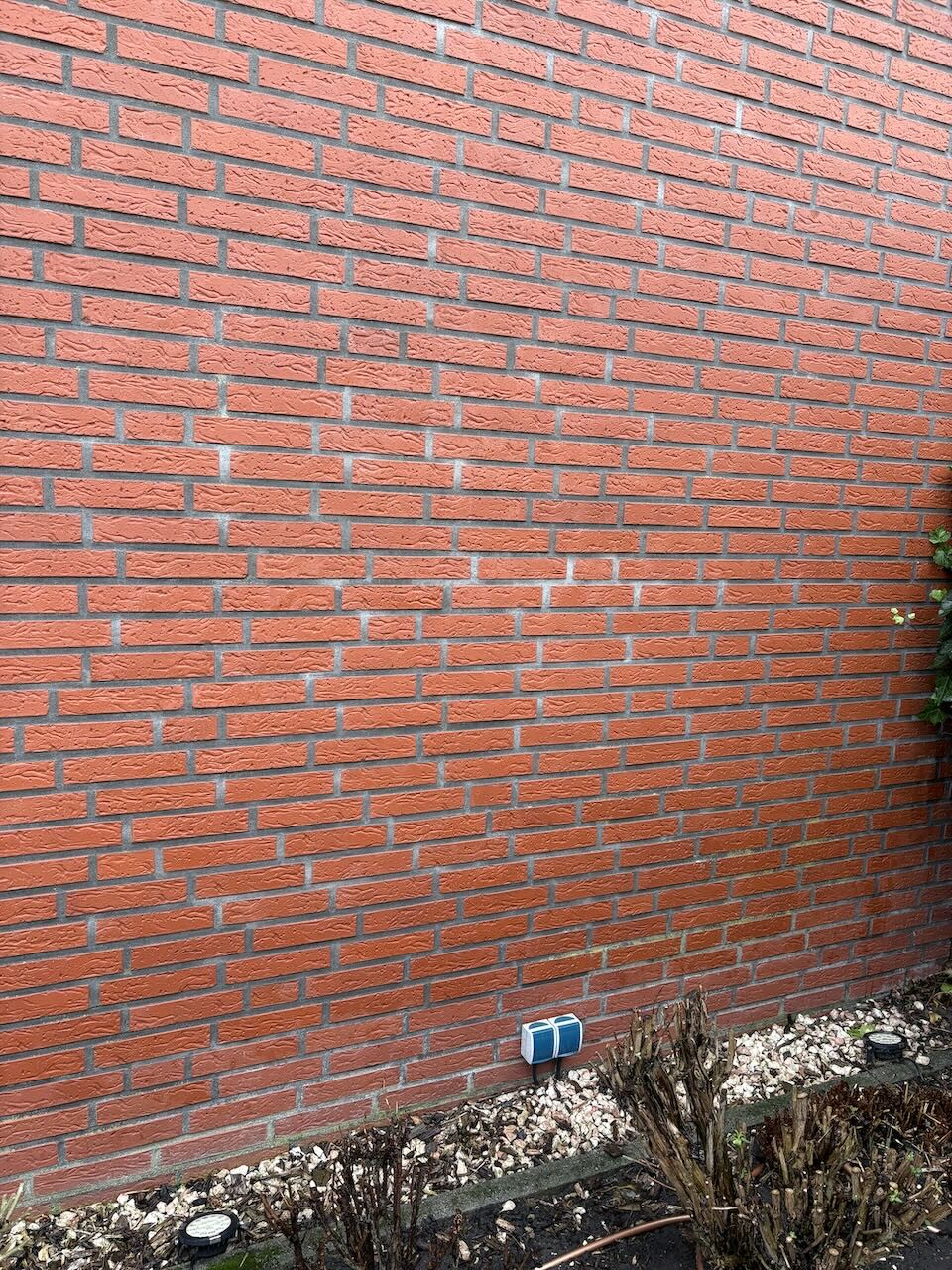 Rote Ziegelwand einer Außenfassade mit Kiesboden und niedrigem Bewuchs.