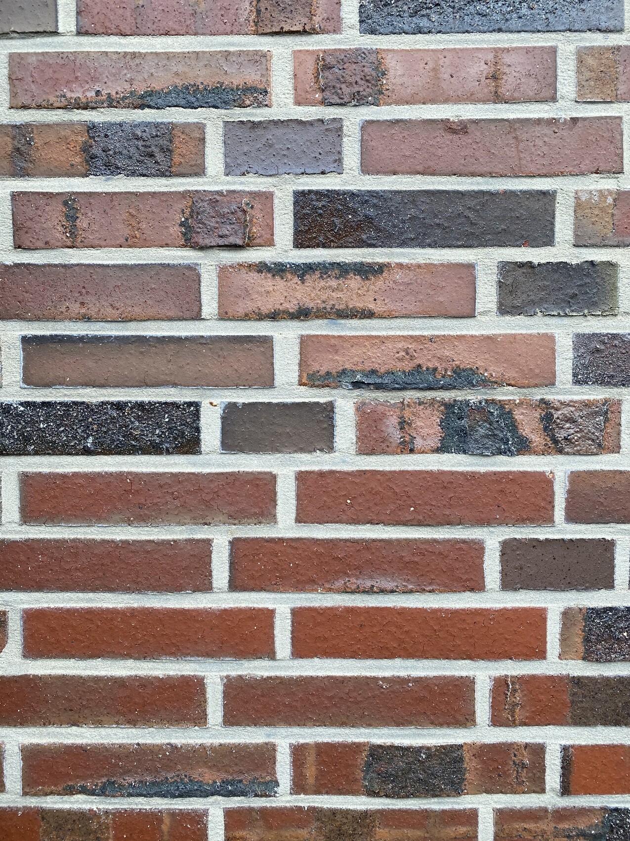 Ziegelwand aus roten und braunen Steinen mit grauem Mörtel.