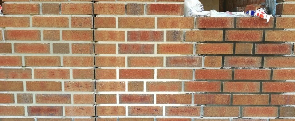 Backsteinmauer mit Müllresten am oberen Rand des Bildes.