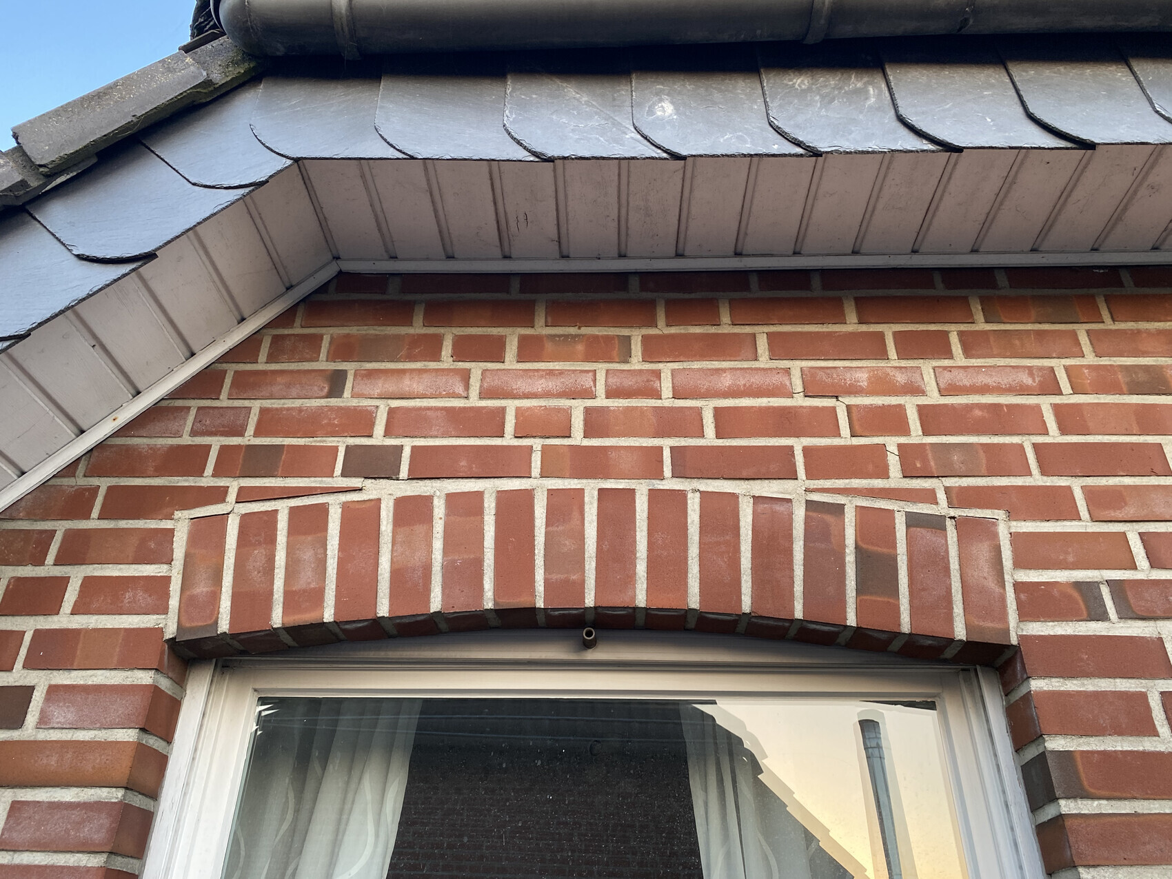 Rote Backsteinwand mit halbrundem Ziegelbogen über dem Fenster und grauer Dachkante