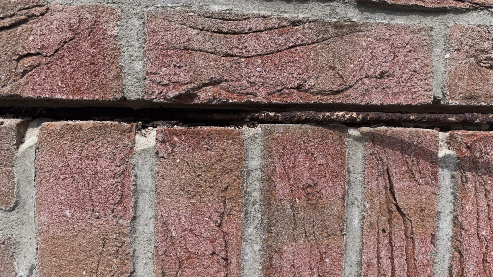 Nahaufnahme einer roten Backsteinwand mit grauem Mörtel und Rissen.