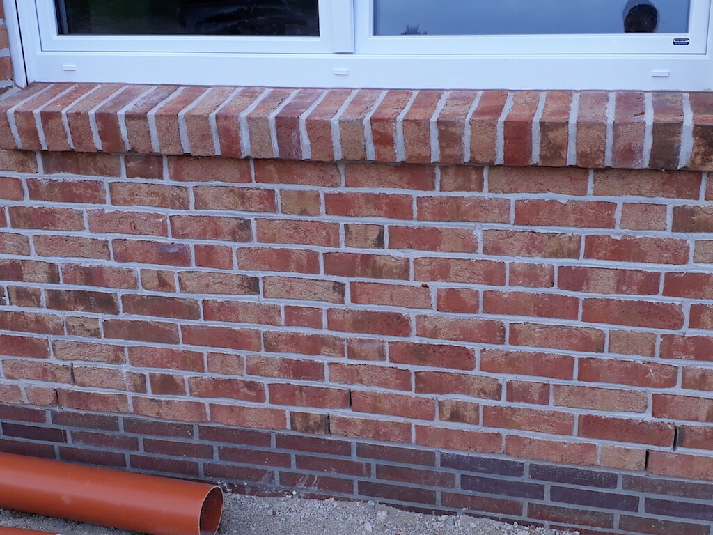 Außenwand aus roten Ziegeln mit Fenster und orangefarbenem Rohr davor.