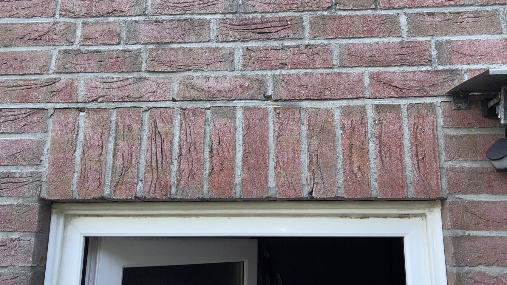 Rote Backsteinwand über weißem Türrahmen; rechts eine Außenleuchte.