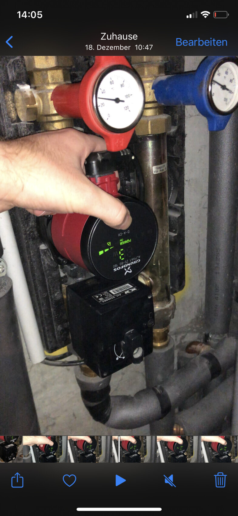 Person bedient roten Pumpenregler; sichtbares Manometer und Rohre der Heizungsanlage.