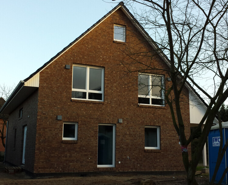 Ziegelhaus mit Satteldach, zwei große Fensterfronten und Baum rechts im Vordergrund.