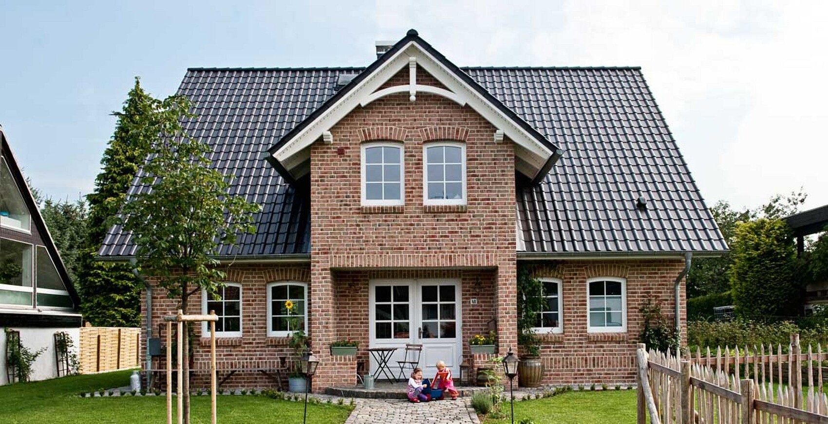 Vorderansicht eines roten Backsteinhauses mit Giebeldach und Garten