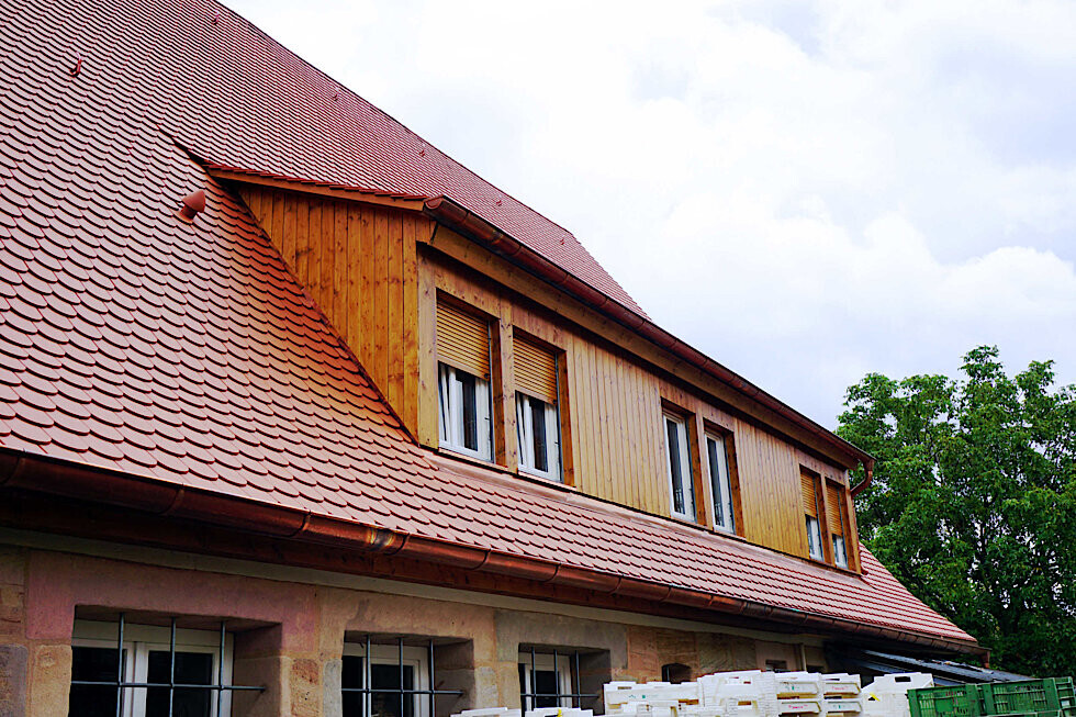 Ansicht eines Hauses mit rotem Dachziegel-Dach und Dachgauben aus Holz