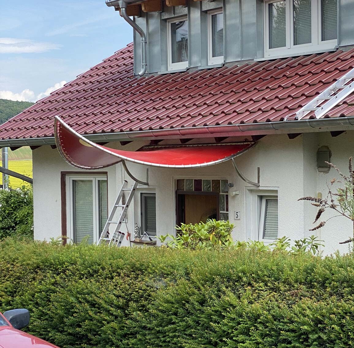 Haus mit rotem Dachziegel, Eingangsvorderseite, Leiter davor und grüne Hecke