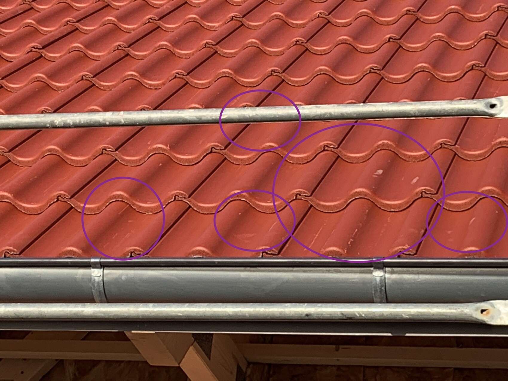 Rotes Ziegeldach mit Wellenziegeln; horizontales Metallrohr darüber, markierte Stellen.