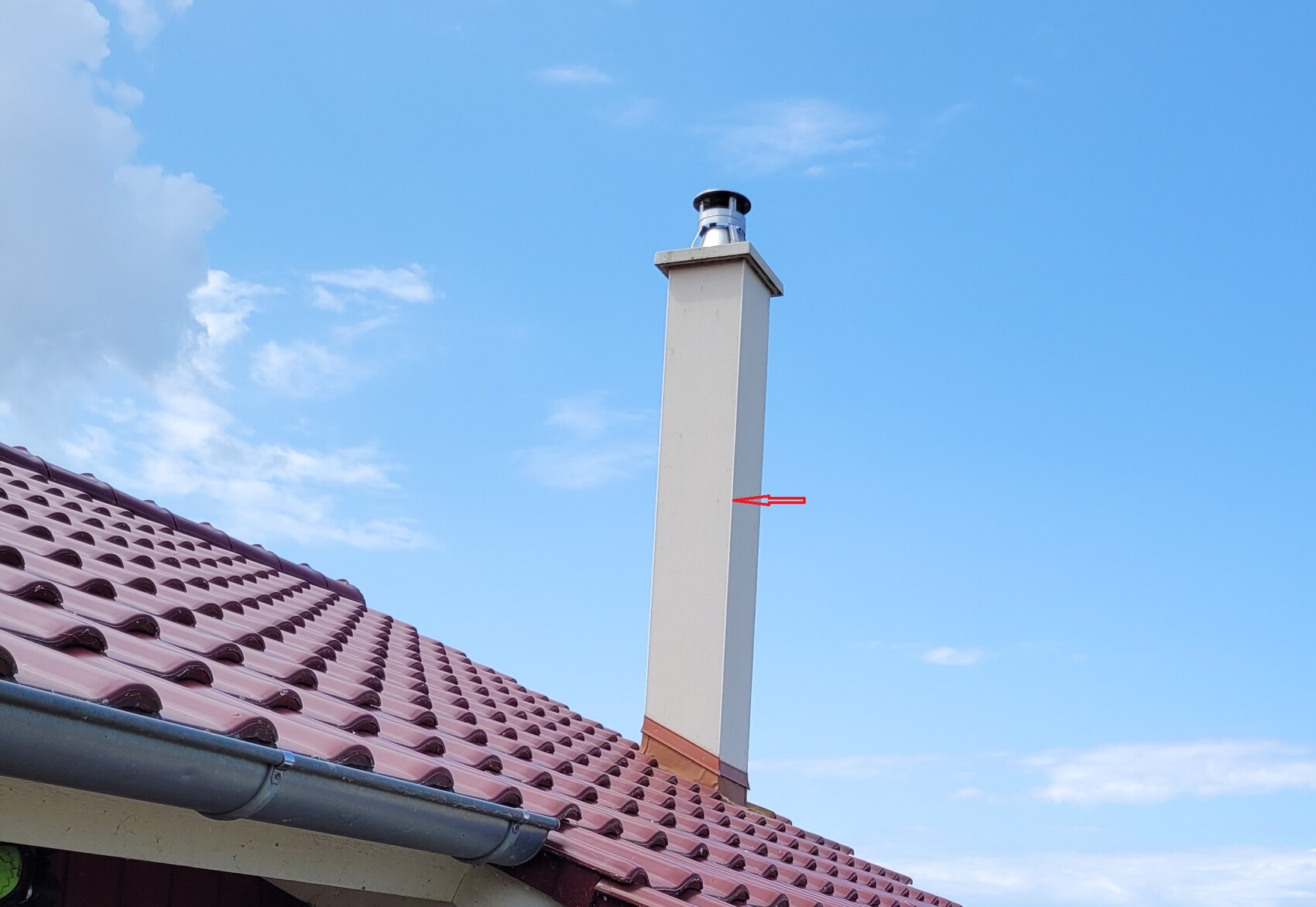 Dach mit rotem Ziegeldach und Kamin unter blauem Himmel.