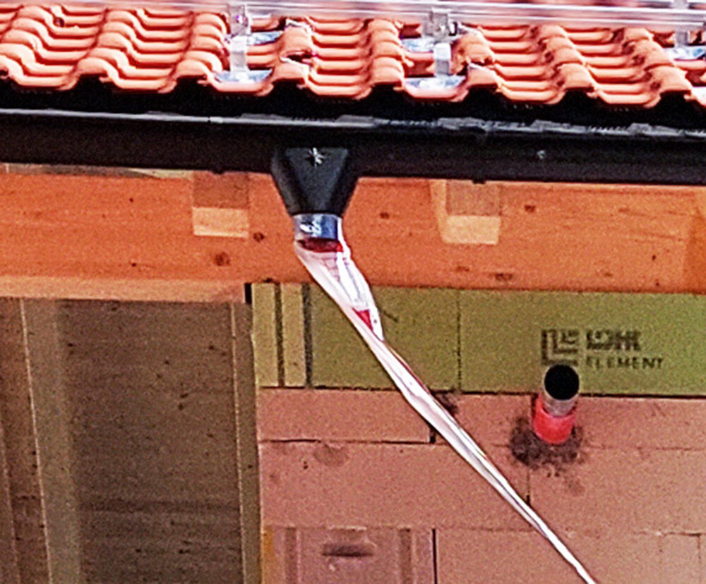 Dach mit roten Ziegeln; von der Dachkante hängt ein weißes Sicherheitsband herab.