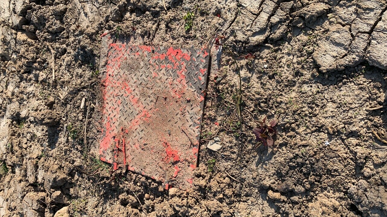 Metallplatte mit Diamantmuster, rot gerändert, liegt auf trockenem, rissigem Boden.