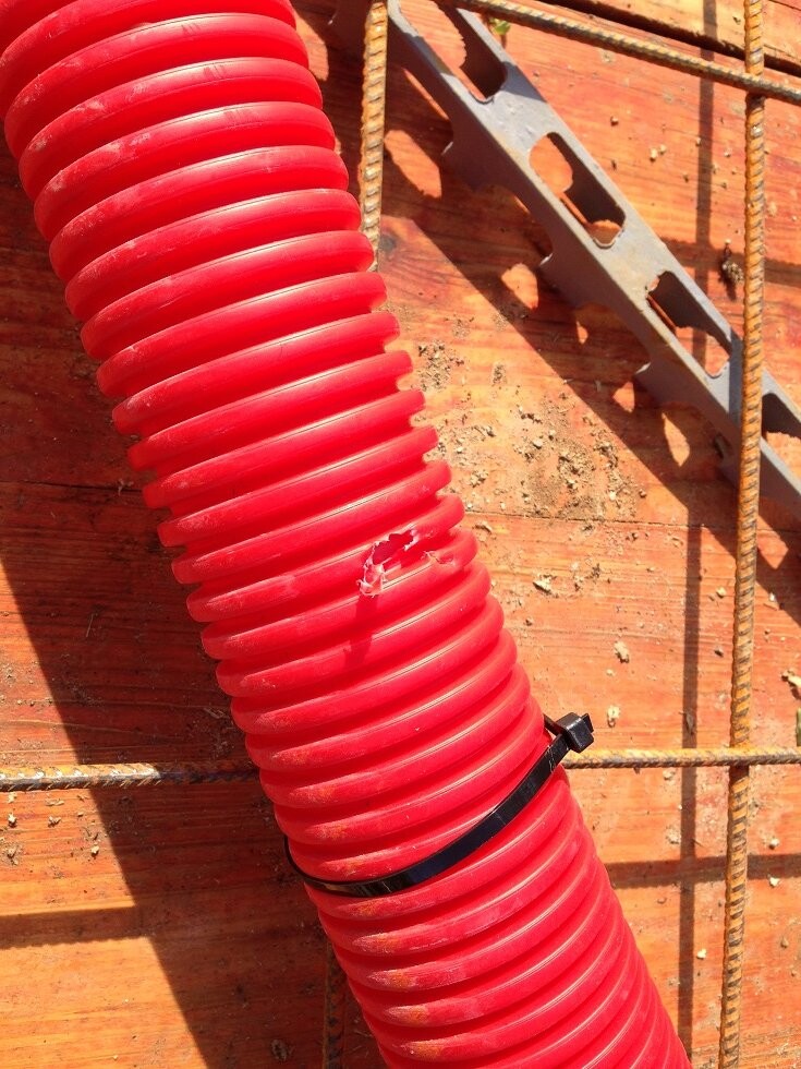 Rotes flexibles Kabelrohr liegt auf Holzuntergrund neben Bewehrungsstahl
