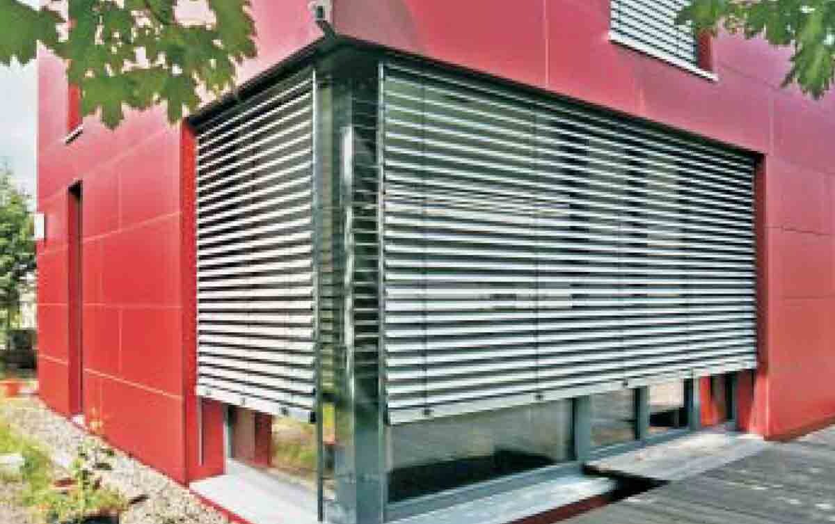 Rotes Gebäude mit großer Fensterfront hinter Metall-Rollläden, modernes Design