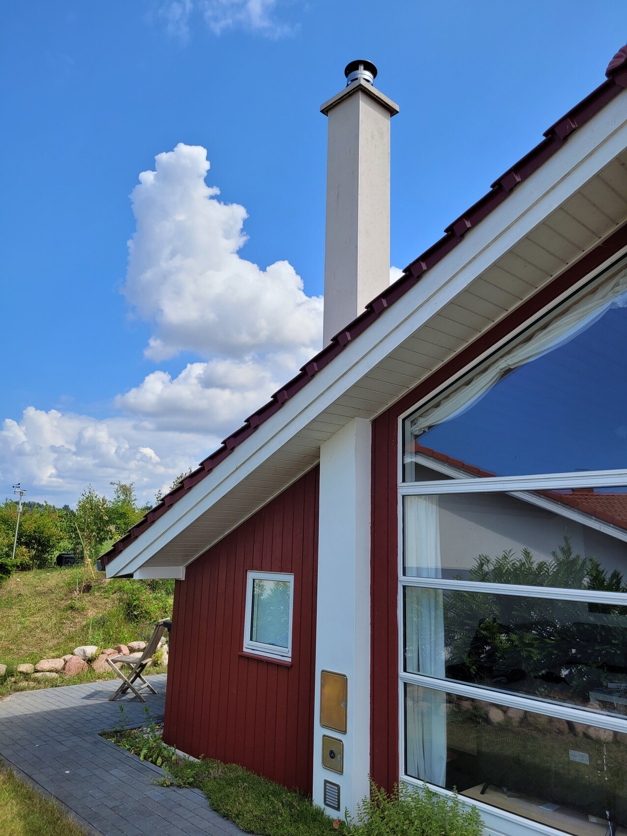 Aussenansicht eines roten Hauses mit schrägem Dach, Kamin und großen Fenstern