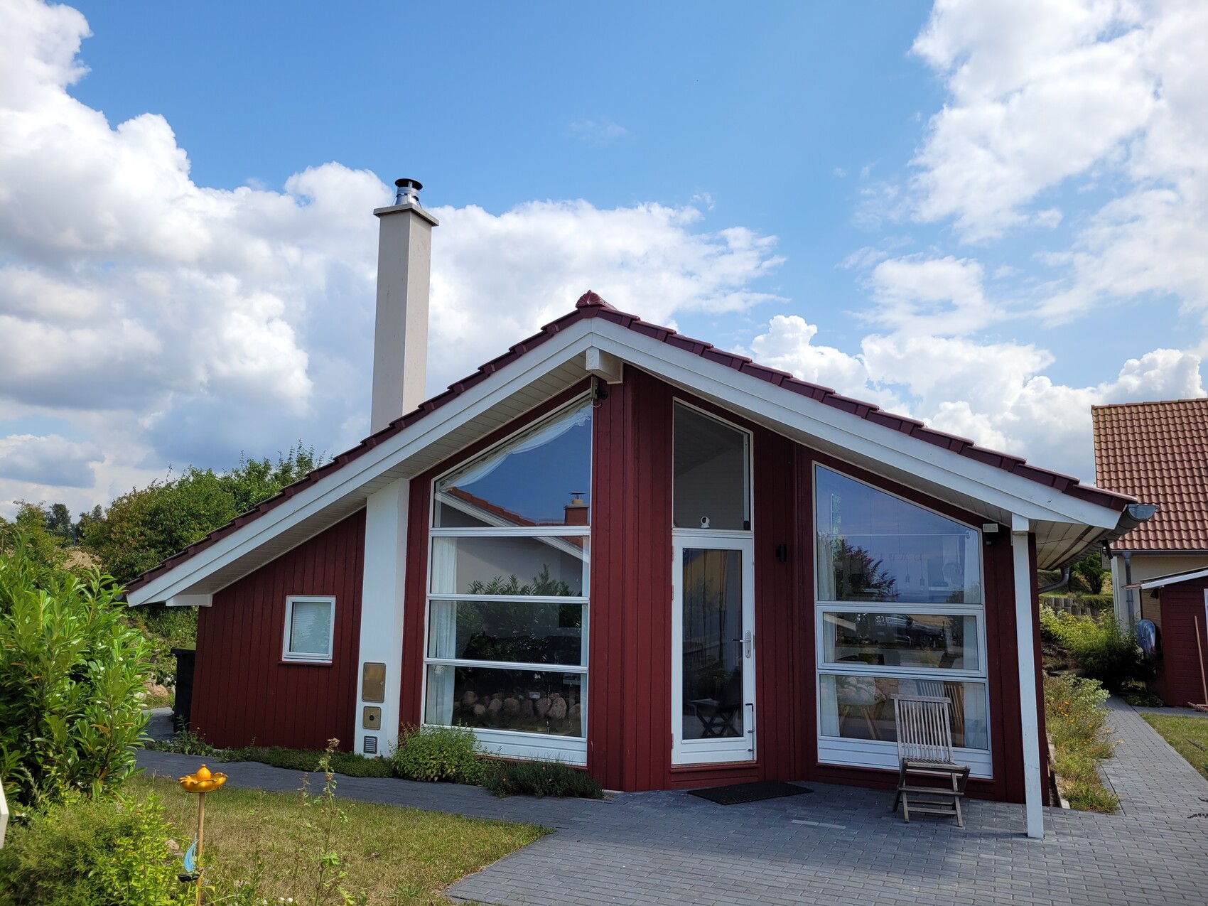 Rotes Holzhaus mit großen Fensterfronten, Kamin und Vorgarten unter blauem Himmel