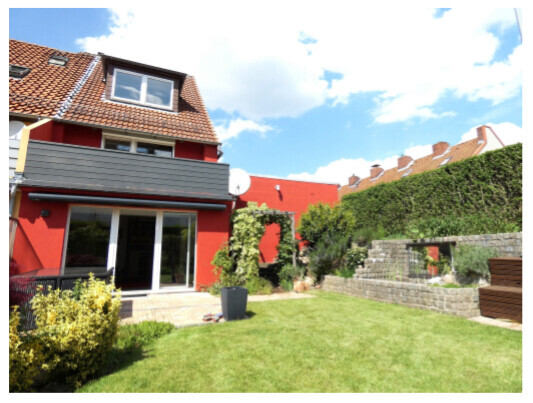 Garten vor rotem Haus mit Terrasse, Rasen, Hecke und Stufen am rechten Rand.
