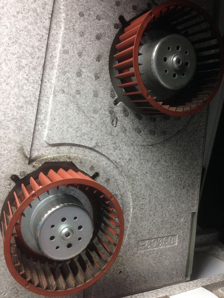 Zwei rote Gebläseräder in grauer Metallvorrichtung, Teil einer Lüftungsanlage.