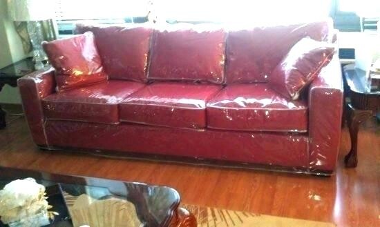 Rotes Ledersofa im Wohnzimmer mit drei Kissen, Glas-Couchtisch und Holzfußboden.