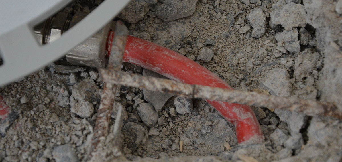 Rotes Rohr im Baugraben mit Erde, Kies und Draht sichtbar