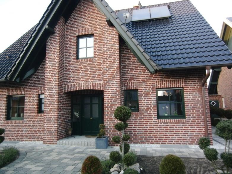 Backsteinhaus mit grünem Eingang, gepflastertem Weg und topiary-Bäumen im Vorgarten.